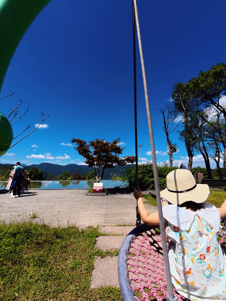 小雨坐在粉色绳网秋千上，面朝山海与蓝天